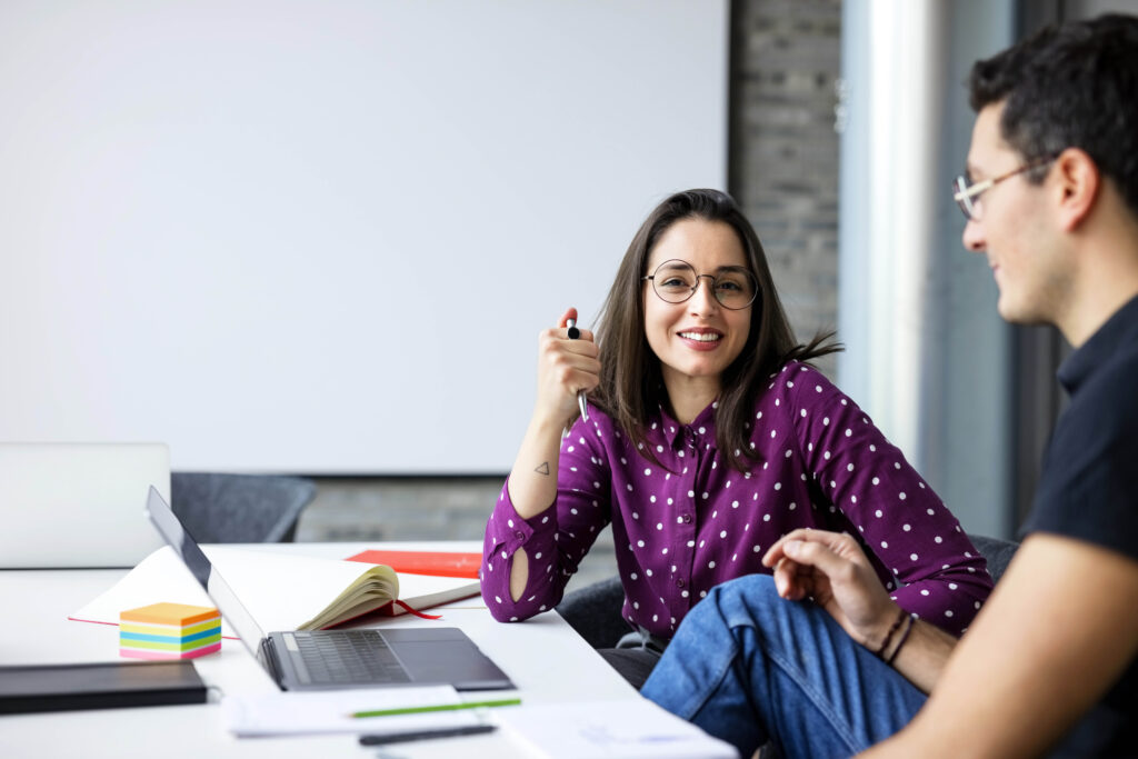 Two coworkers smiling while working together at a boardroom table in a office. Business partners working together in office.