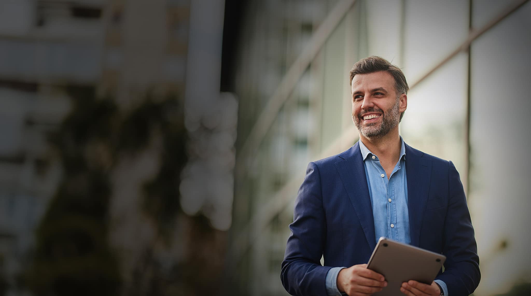 Happy male entrepreneur day dreaming while holding laptop on the street. Copy space.