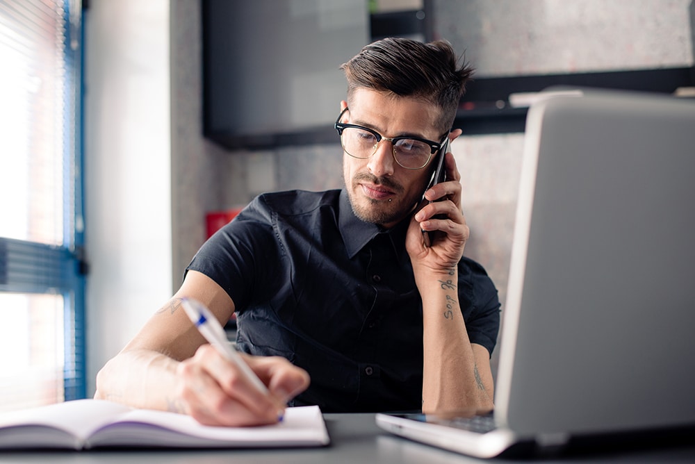 Young man in office working on laptop computer and phone,