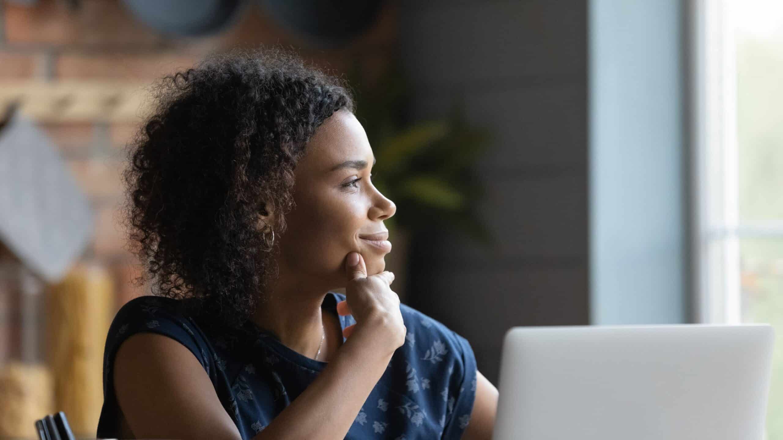 A woman gazing out the window by her laptop